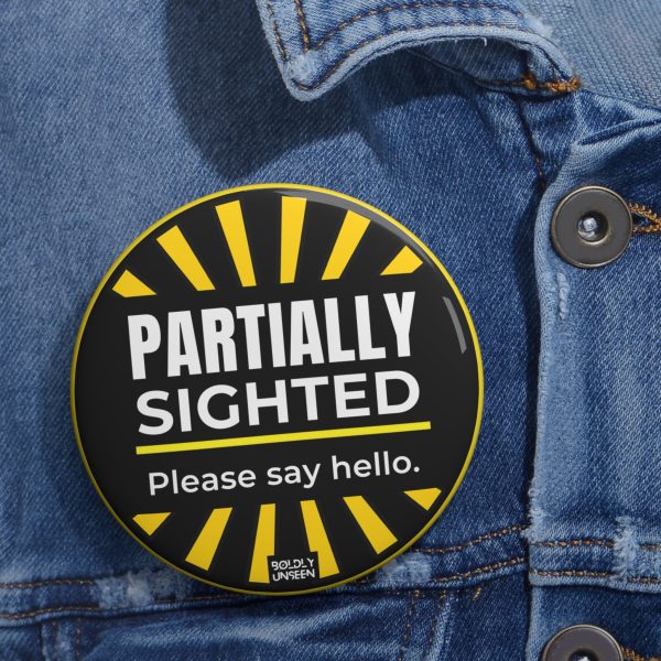 Partially Sighted. Please Say Hello. pin badge pinned on a blue denim jacket, black face, yellow sunburst edge, white lettering